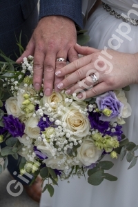 Bride and grooms hands showing their wedding rings posed a bouquet of flowers
