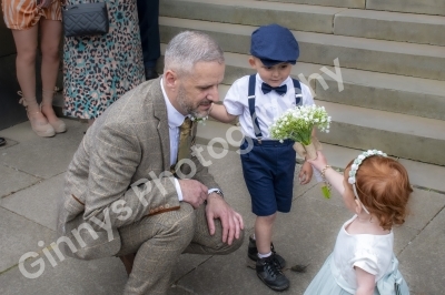 Groom bent down with two young children one of them showing his some flowers