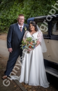bride and groom standing with their wedding car